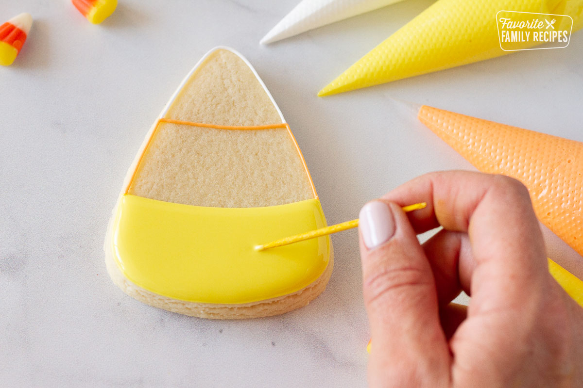 Toothpick swirling yellow royal icing for a Candy corn Halloween cookie.