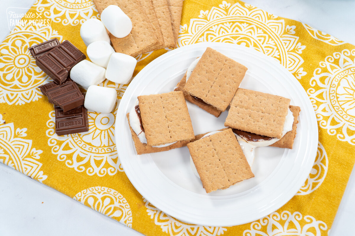 4 Smore's on a plate with chocolate and marshmallows on the side