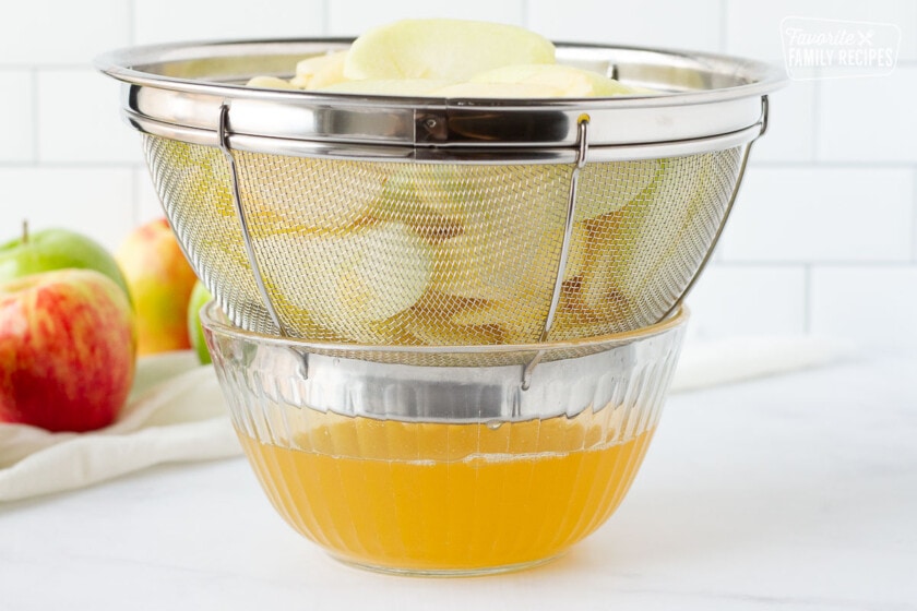 Sliced apples in a colander draining into a bowl for pie filling.
