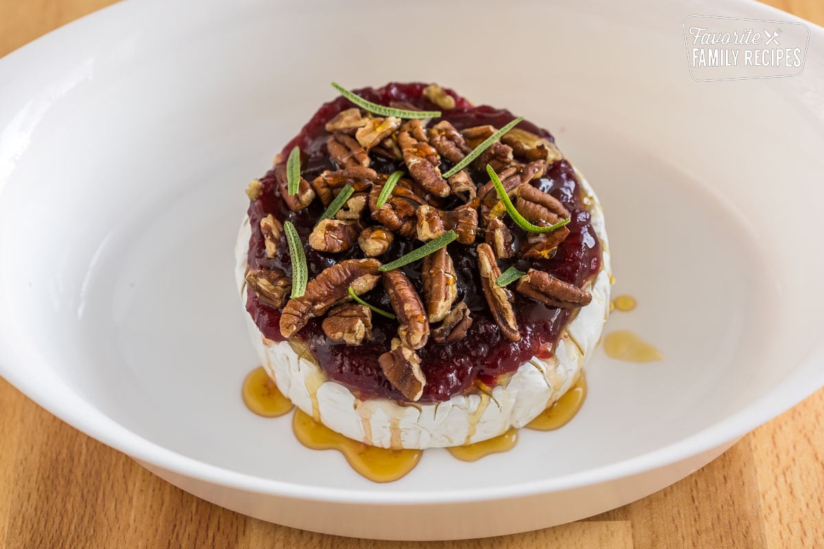 Brie cheese wheel topped with honey, cranberry sauce, pecans, and rosemary