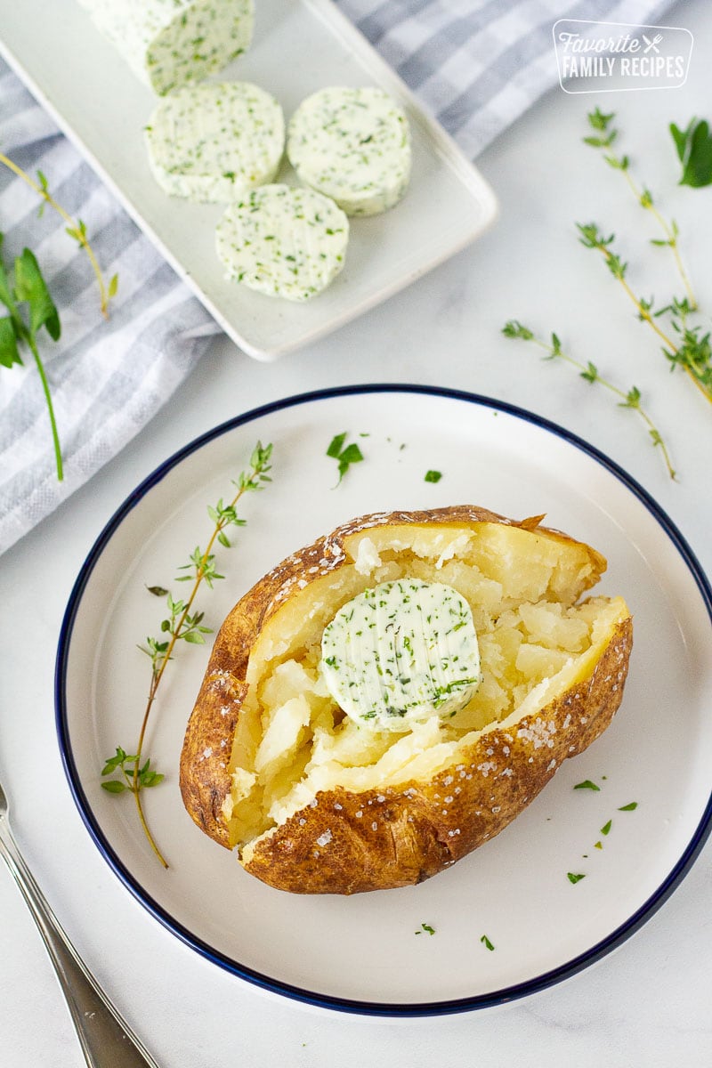 Herbed Butter on a baked potato next to a dish of Herbed Butter discs.