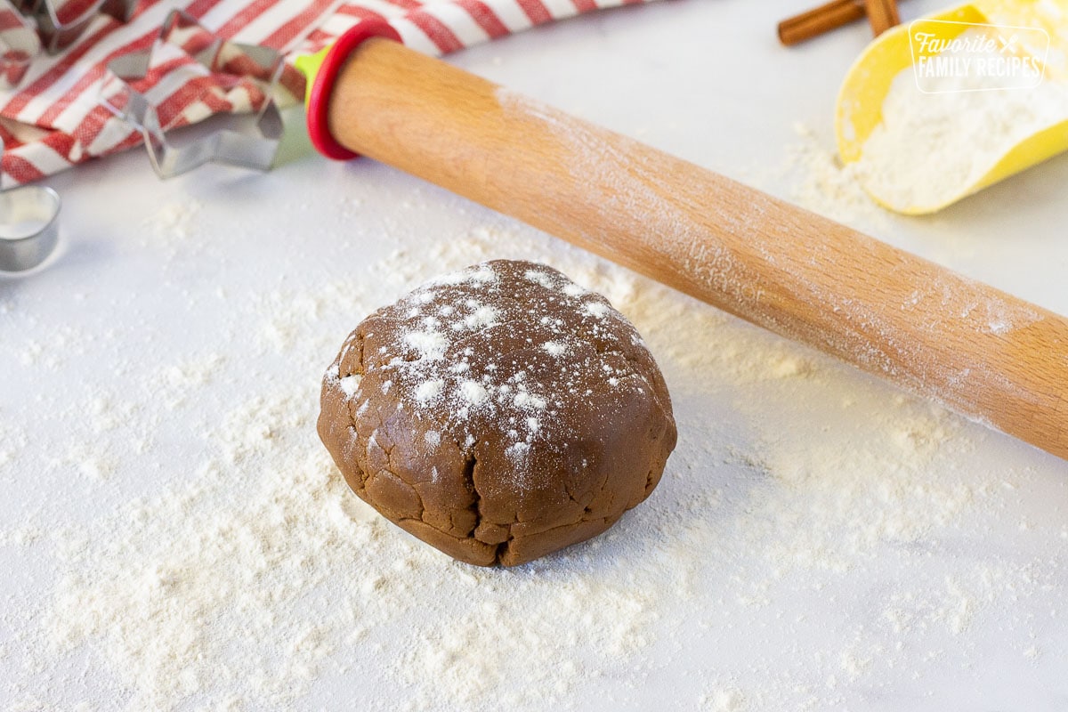 Ball of Gingerbread Cookie dough on a dusted with flour next to a rolling pin.