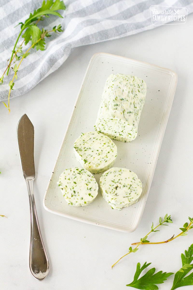 Herbed Butter on a butter dish with a butter knife. Fresh herbs on the side.