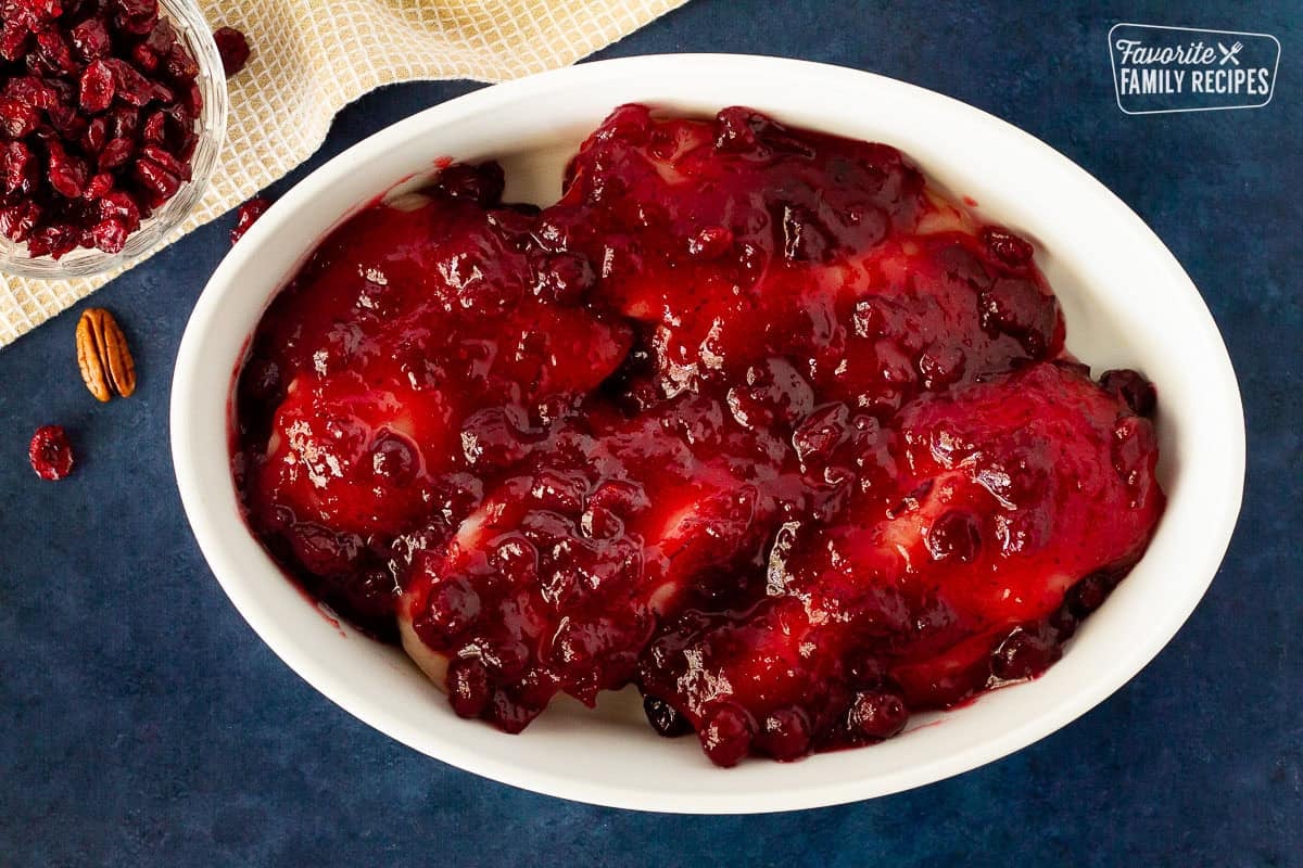 Chicken in a glass dish covered with canned cranberries for Cranberry Chicken.