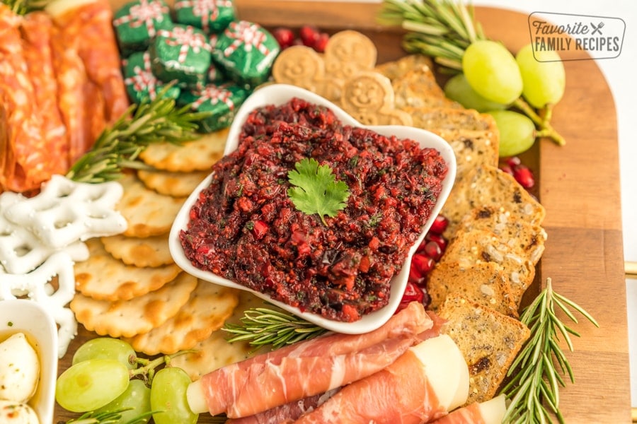 A Christmas Charcuterie Board on a wooden tray with a close up of a bowl of cranberry salsa.
