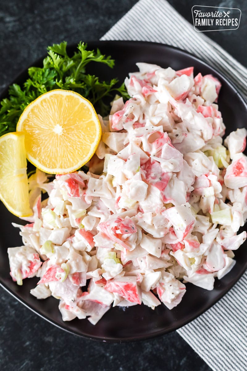 Traditional crab salad on a black plate with lemons and parsley.