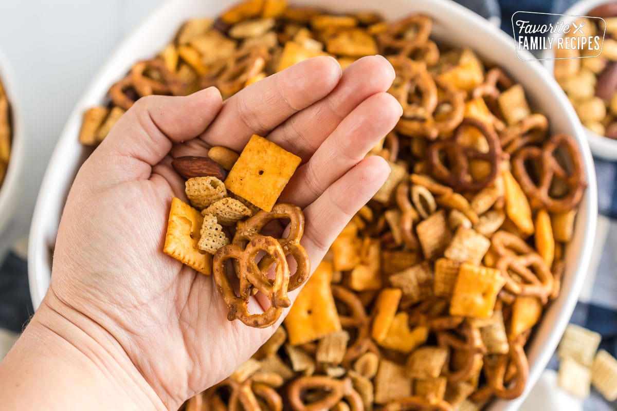 A handful of Chex Mix held above a white bowl. 