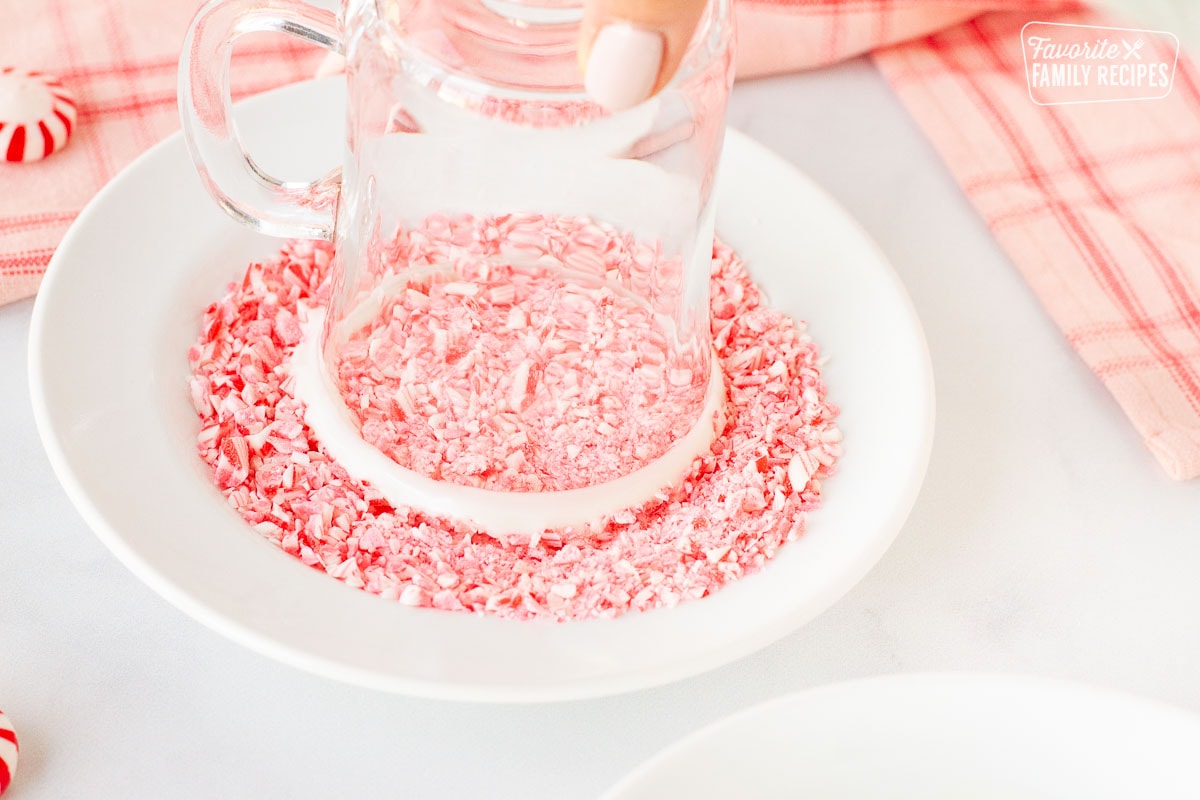 Mug dipped into a plate of crushed candy canes for Peppermint Hot Chocolate.