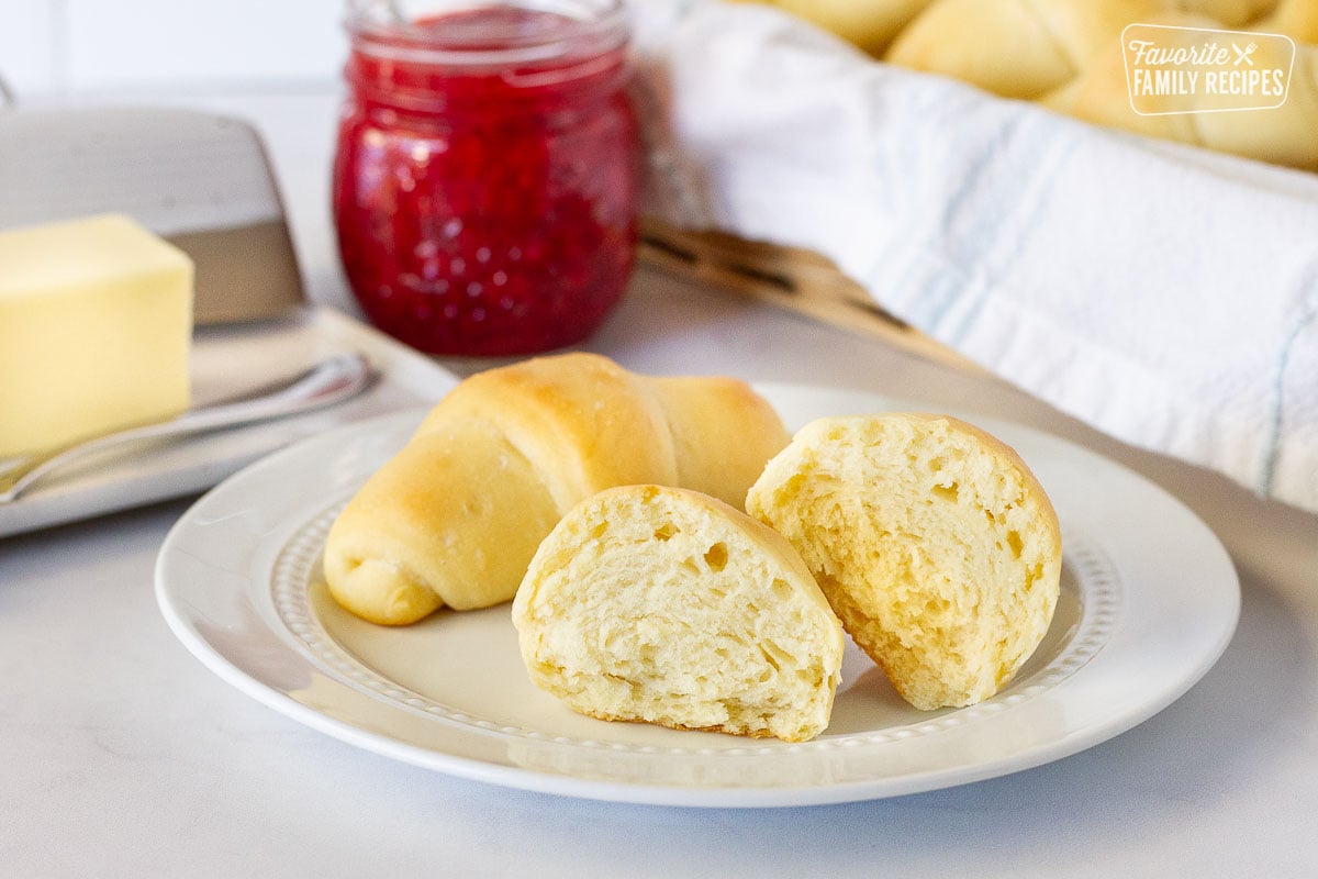 Cut open Homemade Crescent Roll on a plate next to butter and jam in the background.