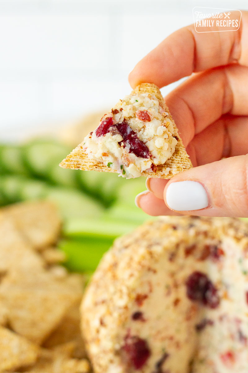 Hand holding triangle crackers with Cranberry Almond Bacon Cheese Ball on top.