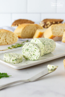 Sliced Herbed Butter on a dish with a butter knife and bread.