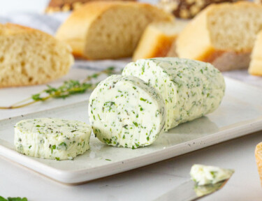 Sliced Herbed Butter on a dish with a butter knife and bread.