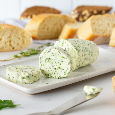 Sliced Herbed Butter on a dish with a butter knife and bread.