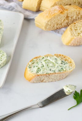 Herbed Butter spread on sliced bread next to a butter dish with sliced Herbed Butter.