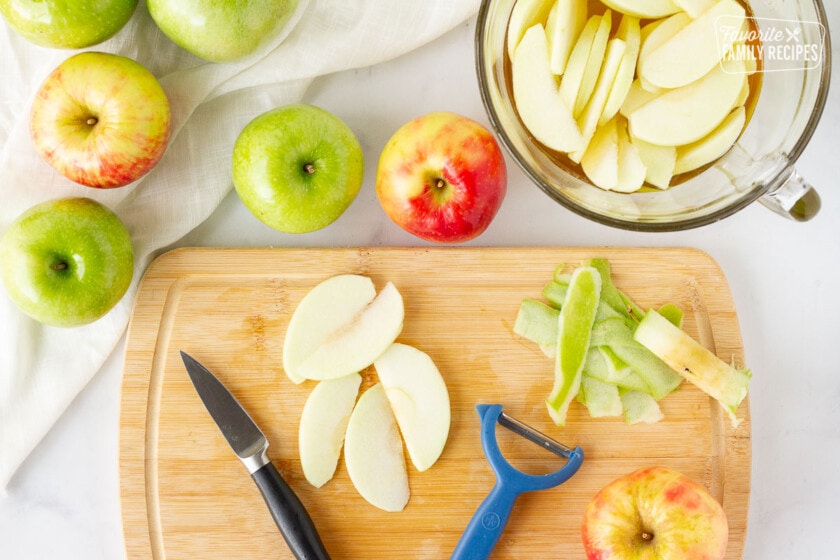 Apples peeling and slicing on a cutting board for Homemade Apple Pie filling.