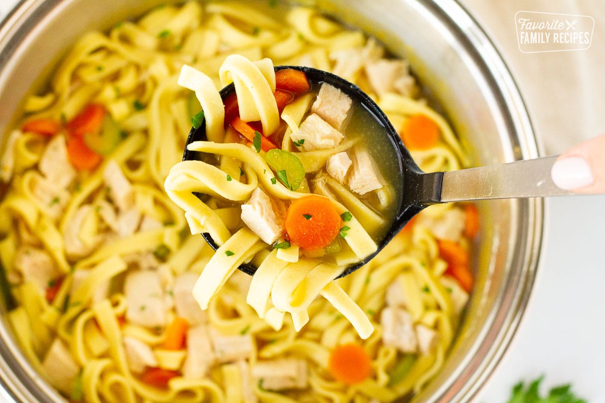 Ladle holding a scoop of Homemade Chicken Noodle Soup.