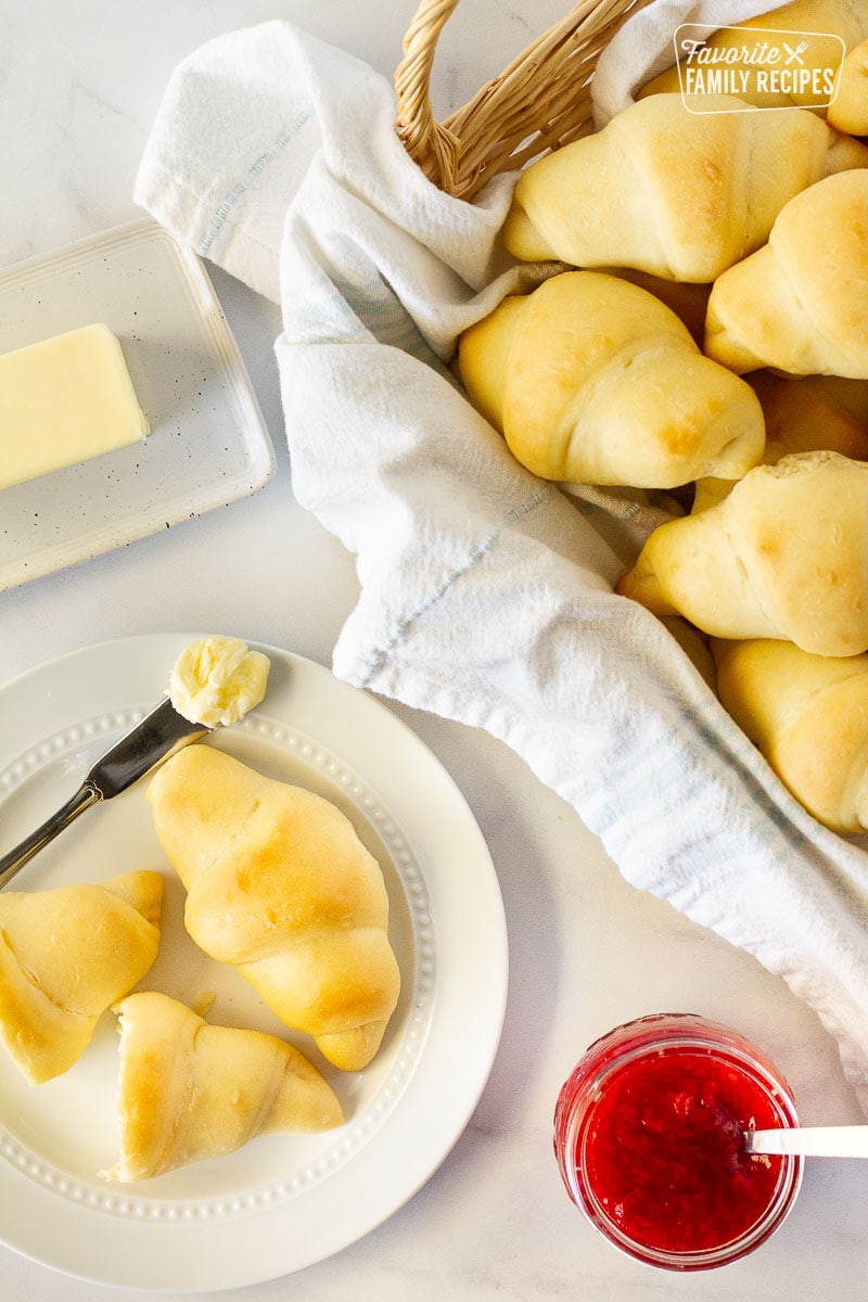 Top view of Homemade Crescent Rolls on a plate and in a basket. Jam and butter on the side.