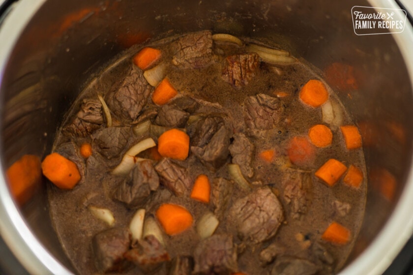 An Instant pot with beef, carrots, onion, and broth
