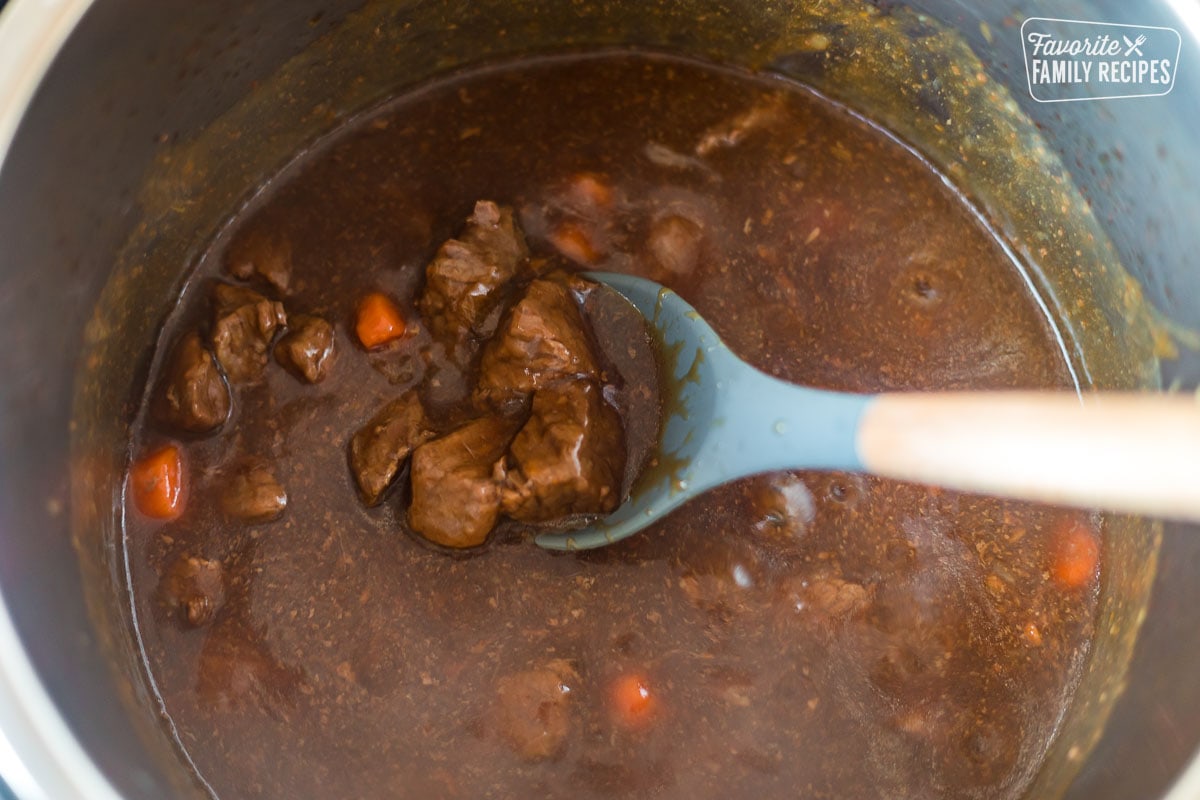 A spoon holding tender, cooked beef chunks in a large pot
