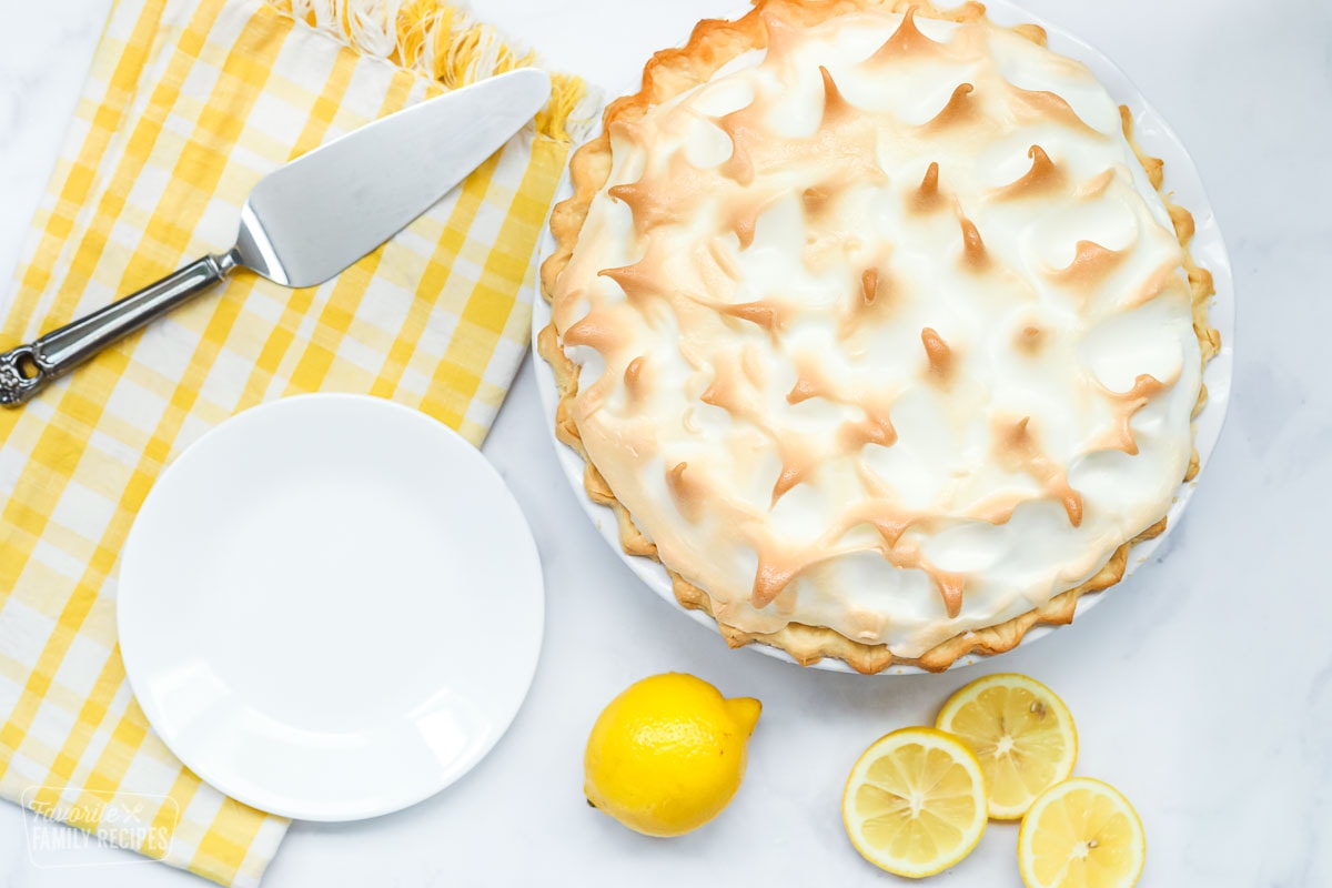 A lemon meringue pie with a plate, lemons, and lemon slices