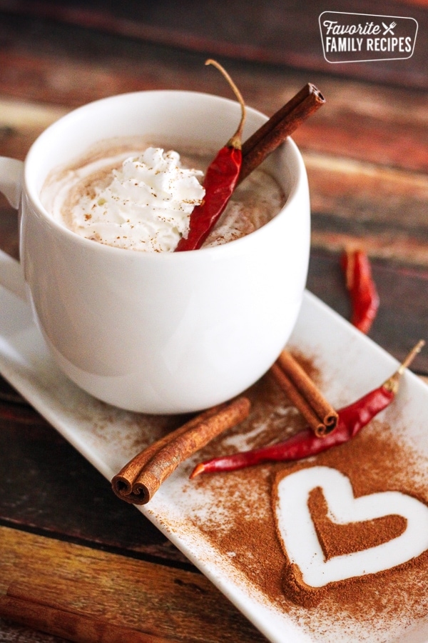 Mexican hot chocolate with chili in the white mug with a heart in the cinnamon on the serving platter. 