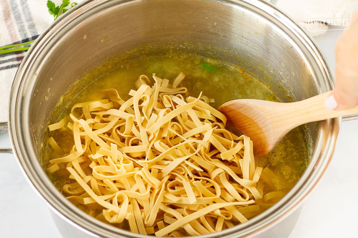 Dry noodles in pot of Homemade Chicken Noodle Soup.