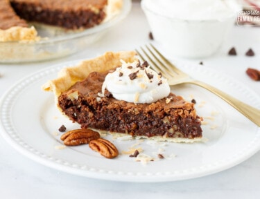 German Chocolate Pie slice on a plate topped with whipped cream, toasted coconut and chocolate.