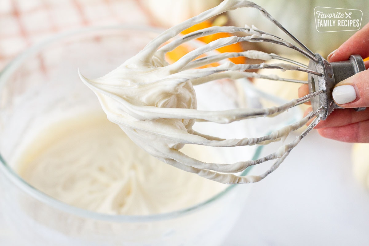 Cream cheese frosting on a mixing whisk for Pumpkin Bundt Cake.