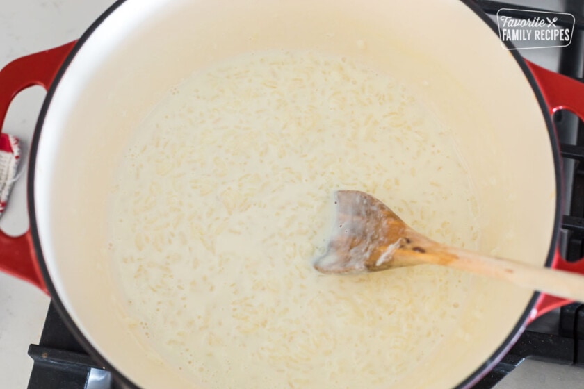 Arborio rice in a Dutch oven with milk being stirred