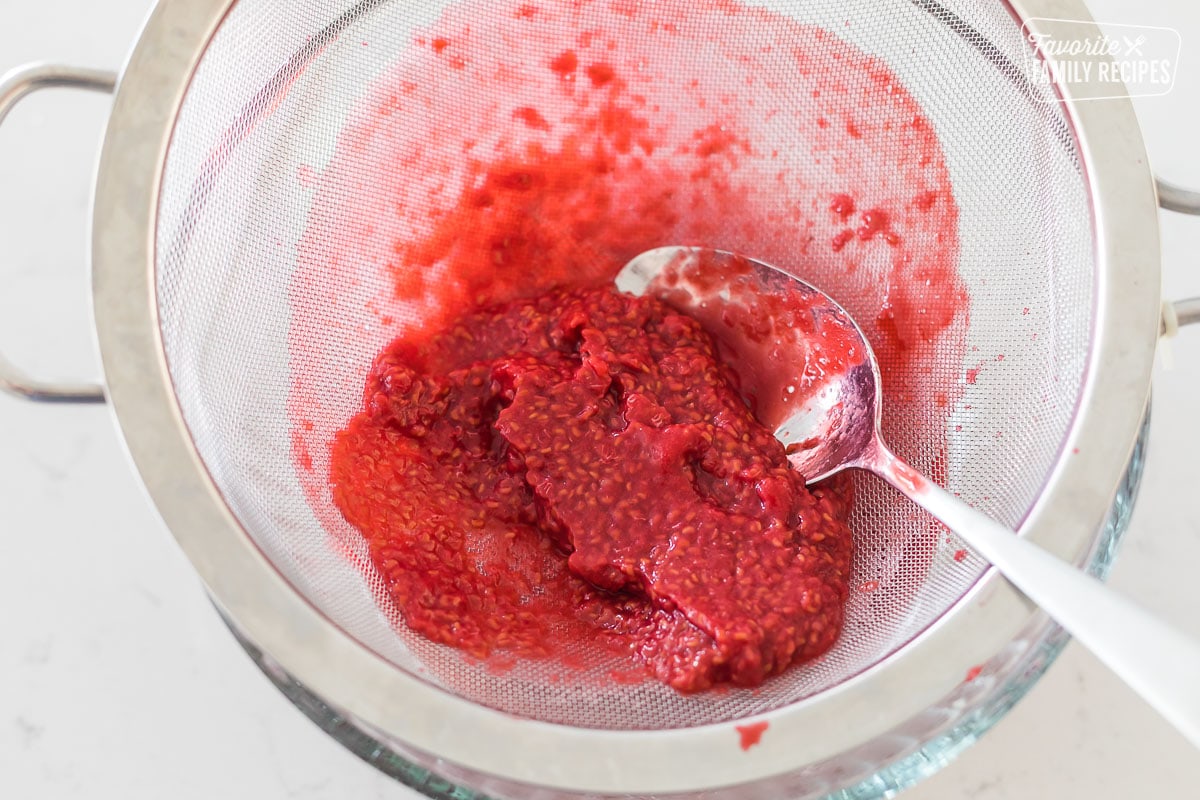 Raspberries being pressed through a strainer to remove seeds