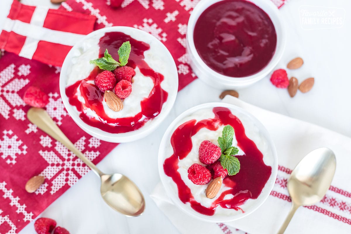 Risalamande (or Ris a la mande) is a Danish rice pudding that is served around Christmastime. This creamy, sweet pudding is a delicious dessert that everyone will love, whether or not you have Danish roots! Two bowls of risalamande next to a bowl of raspberry sauce