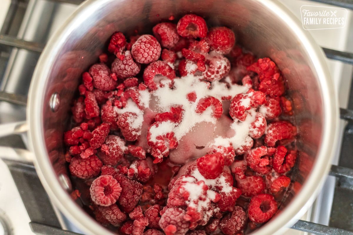 Frozen raspberries in a saucepan with sugar