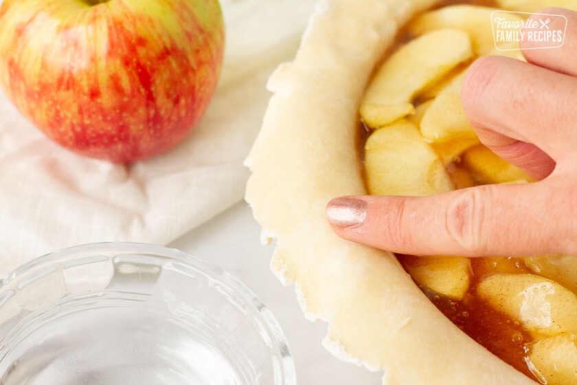 Finger with water rubbing around Apple Pie shell.