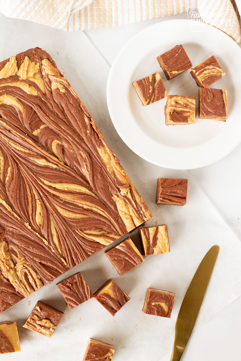 Whole brick of Chocolate Peanut Butter Fudge with cut up pieces next to a plate of Chocolate Peanut Butter Fudge pieces.