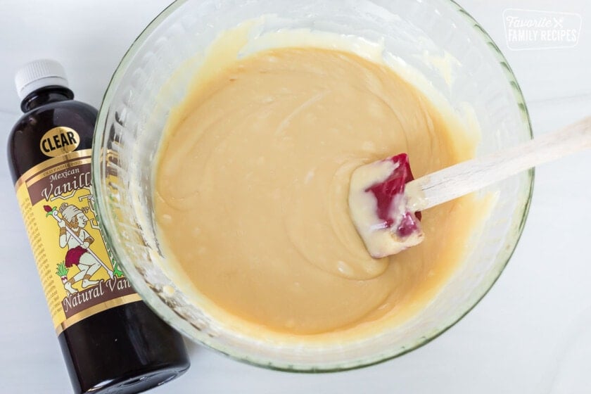 Melted white chocolate chips in a bowl next to a bottle of vanilla