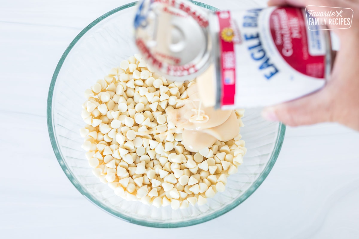 Sweetened condensed milk being poured into a bowl of white chocolate chips