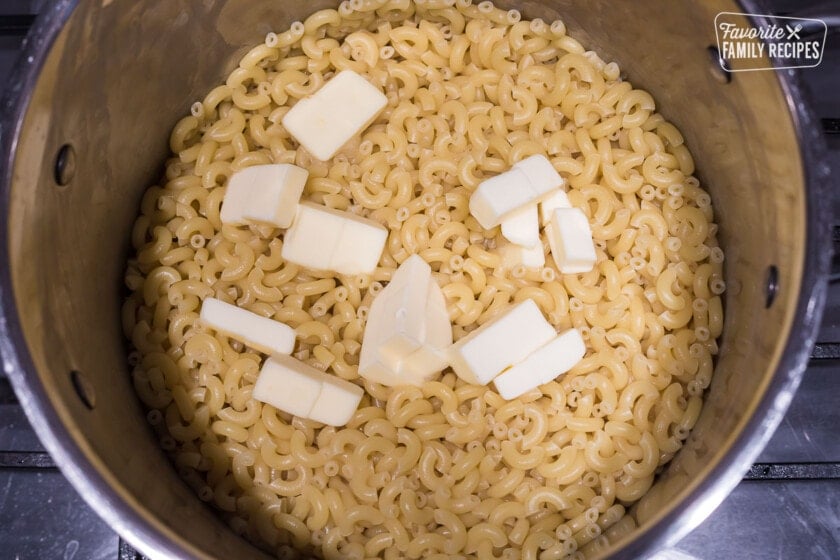 Cooked elbow macaroni in a large pot with cubes of butter over the top