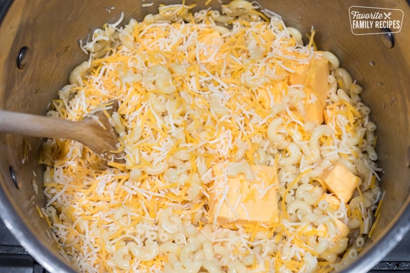 Macaroni noodles in a large pot with shredded cheese and Velveeta cheese