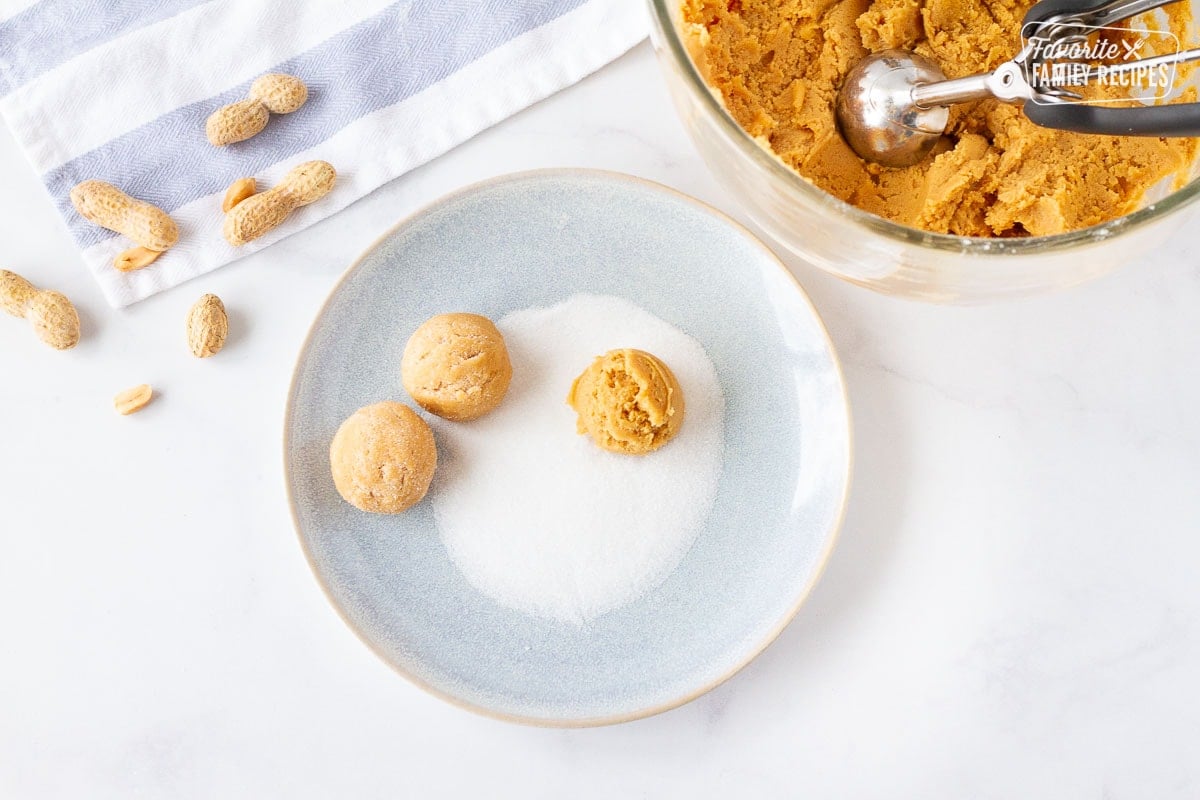 Balls of Peanut Butter Cookie dough on a plate of sugar.