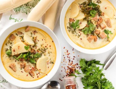 Two bowls of Zuppa Toscana next to breadsticks