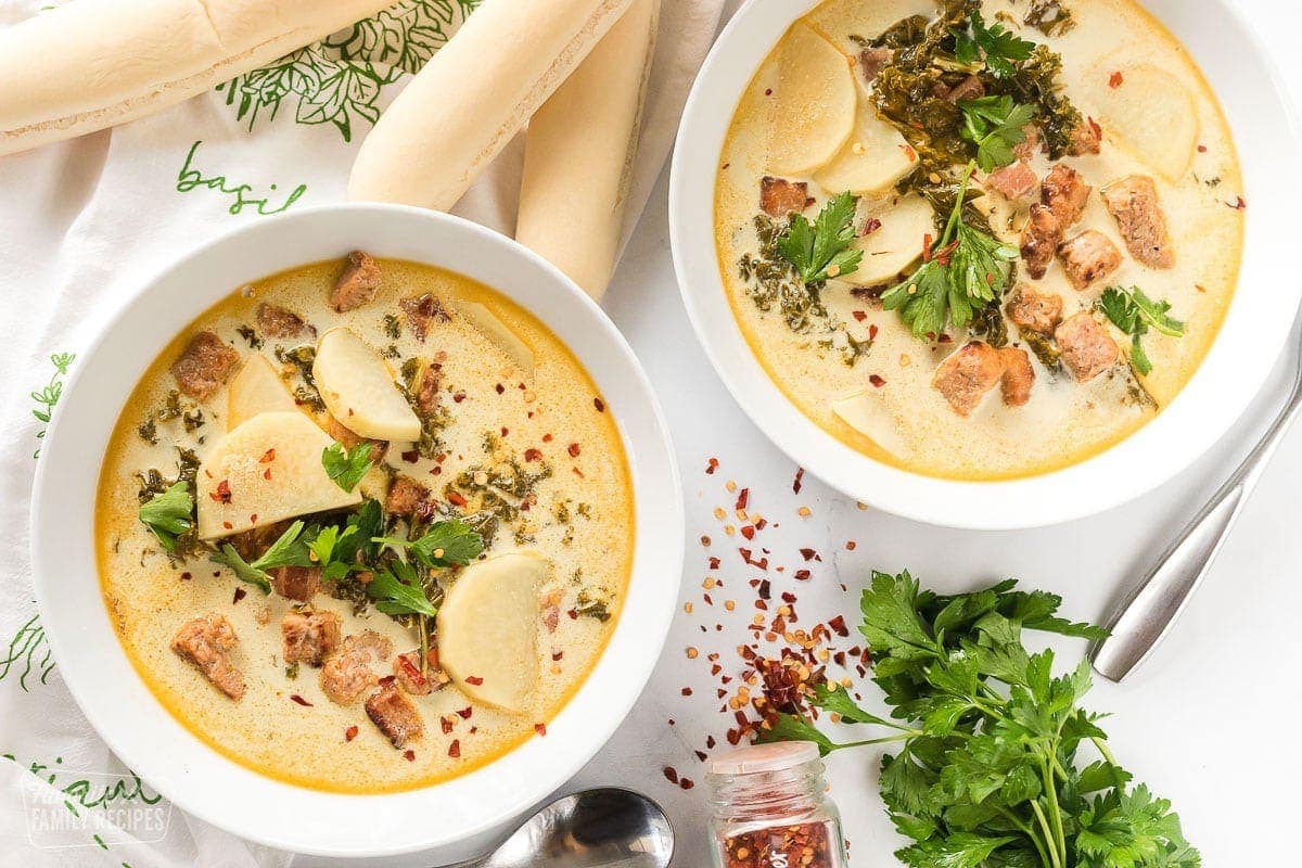 Two bowls of Zuppa Toscana next to breadsticks