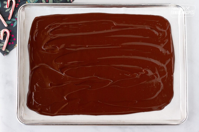 Pan of chocolate spread on parchment paper for Peppermint Bark.