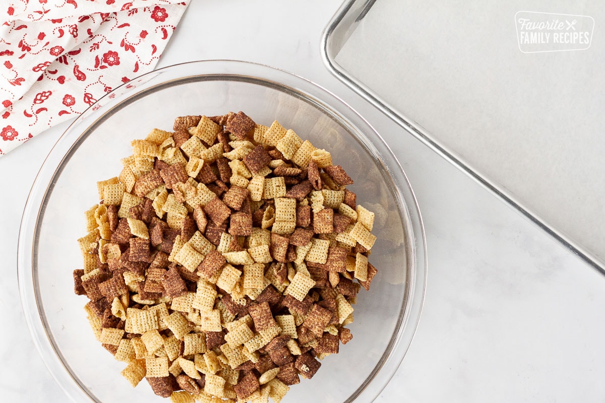 Bowl of chocolate Chex and baking pan with parchment paper to make Sweet Chex Mix.