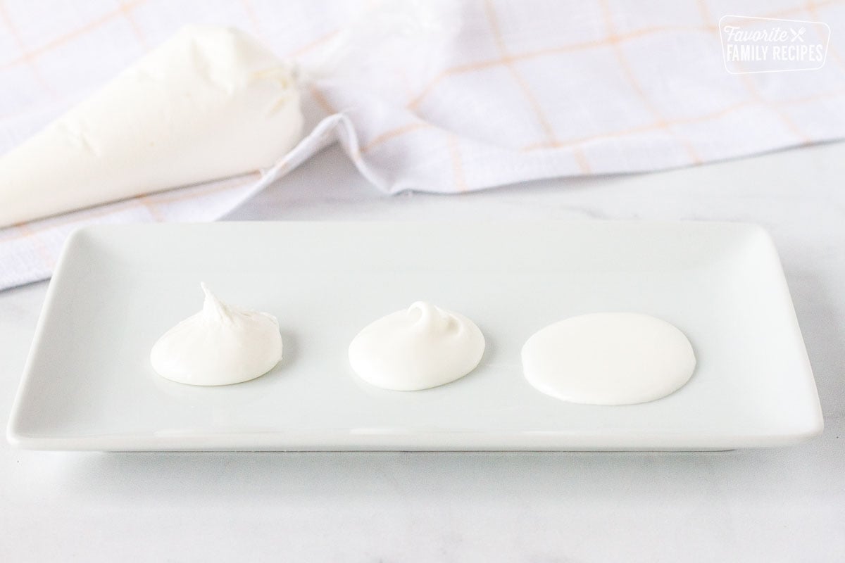 Three royal icing consistencies on a plate next to a bag of royal icing.