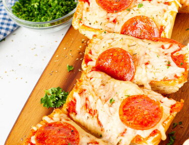 French Bread Pizza cut into slices on a cutting board.