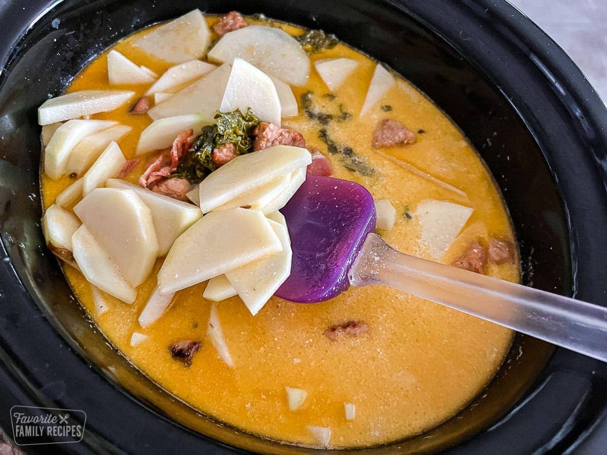 Potatoes being stirred into a Crockpot of Zuppa Toscana