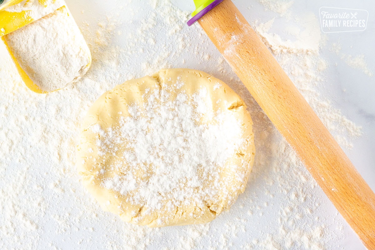 Floured surface with a disc of Christmas Sugar Cookie dough next to a rolling pin.