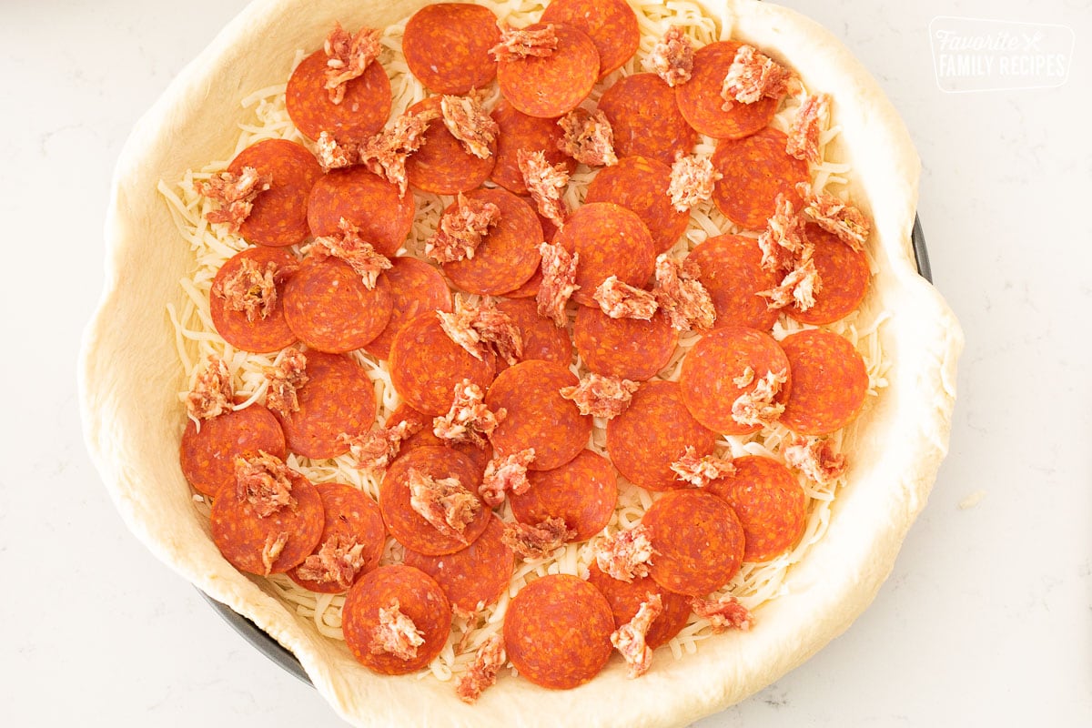 An uncooked deep dish pizza with cheese, pepperoni, and sausage