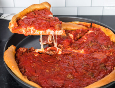 A slice of Chicago style deep dish pizza being lifted from a deep dish pan