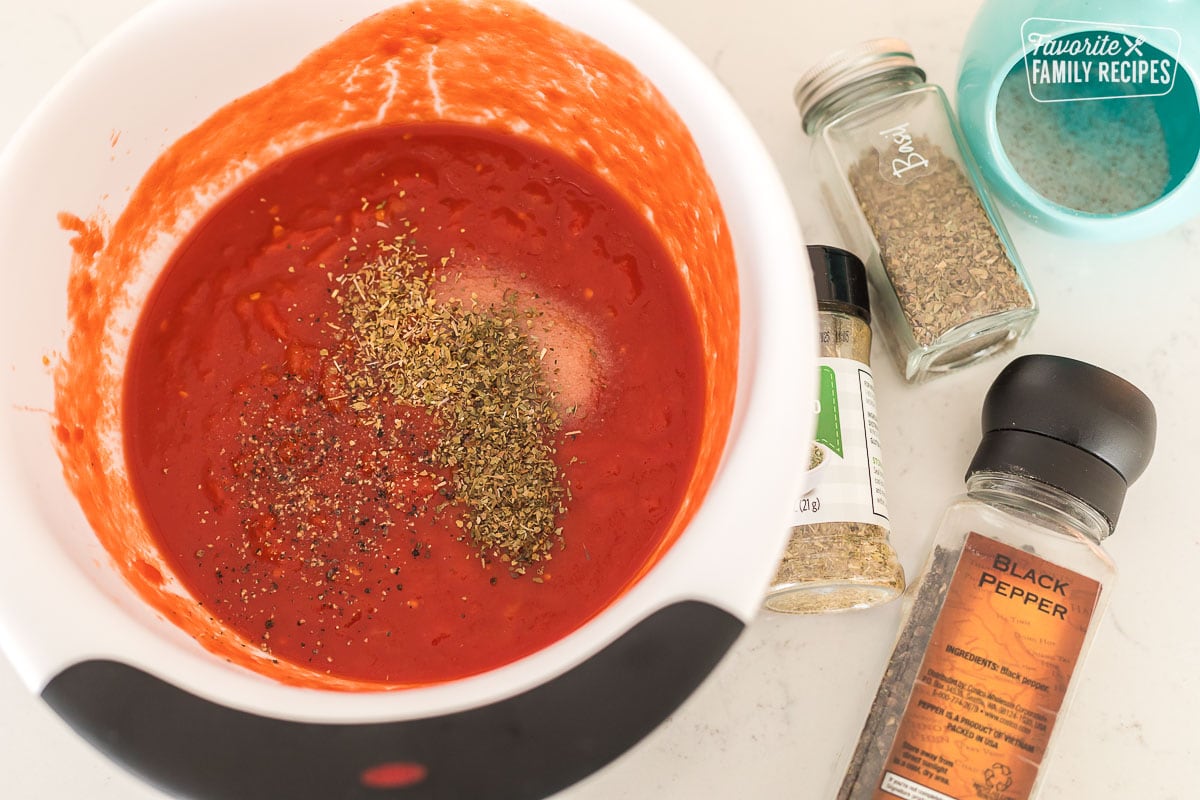 A bowl of tomato sauce with seasonings sprinkled over the top